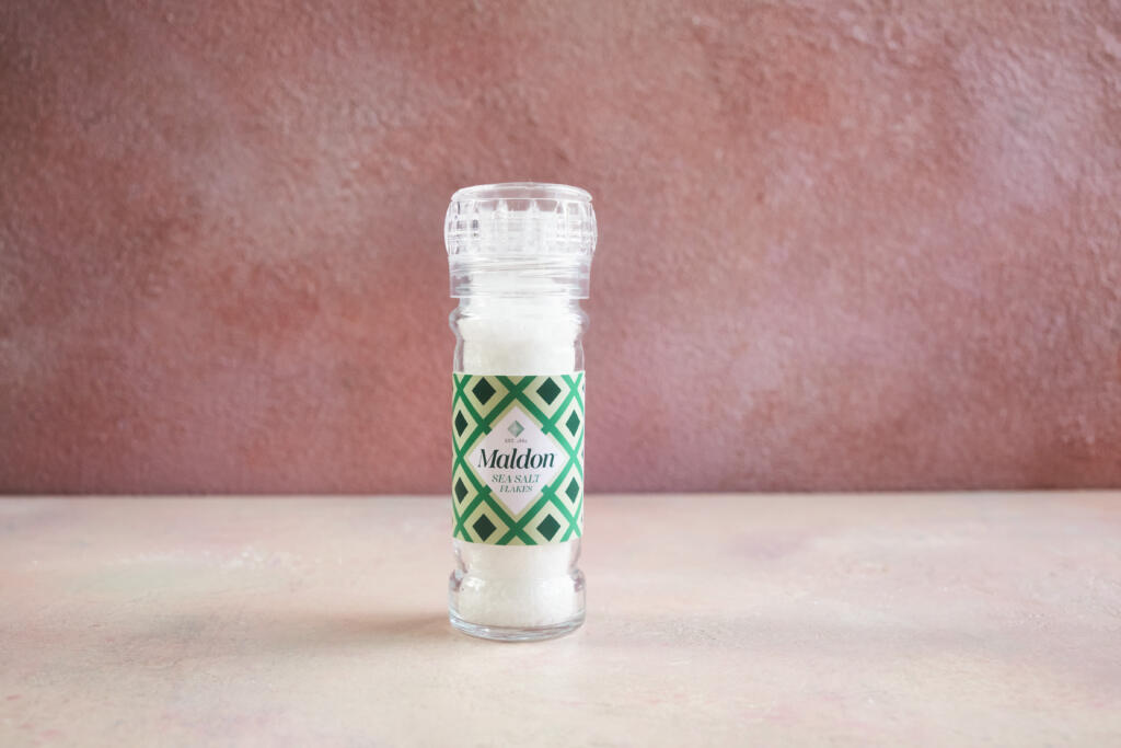 Maldon Original Sea Salt 55g grinder. Pink background.