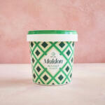 Maldon Original Sea Salt 570g tub. Pink background.