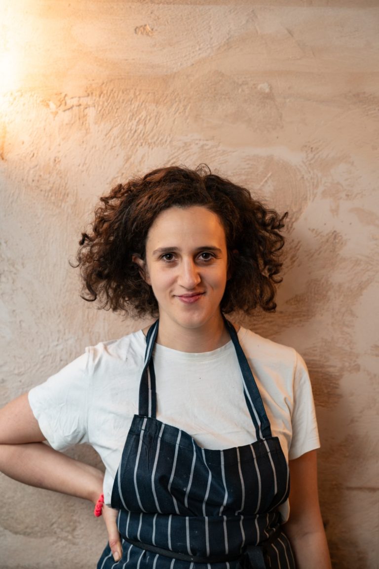 Helen stands smiling in front of a textured beige wall.