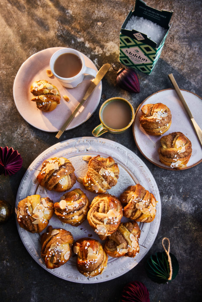Two plates of orange and almond buns with two mugs of coffee.