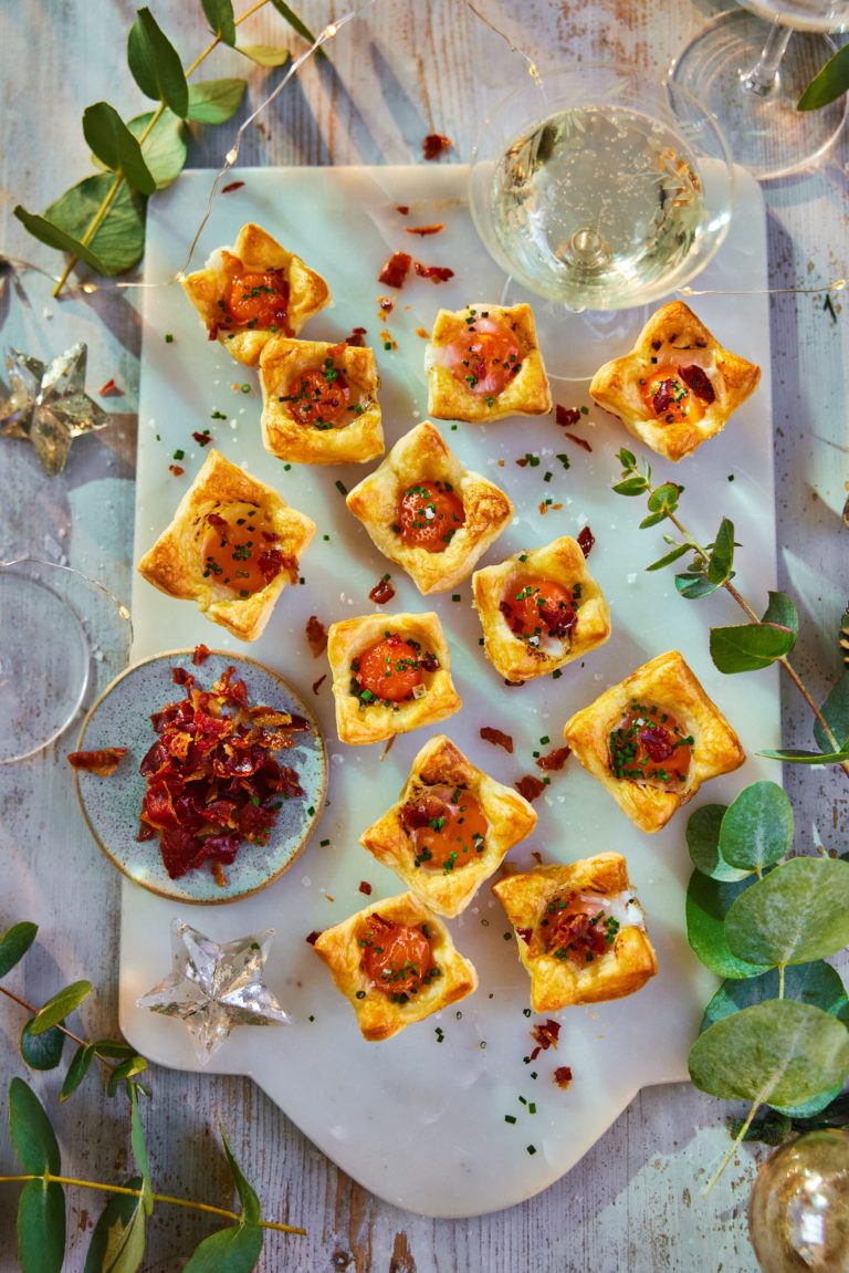 Several quail eggs in blankets pastries on a decorated board.