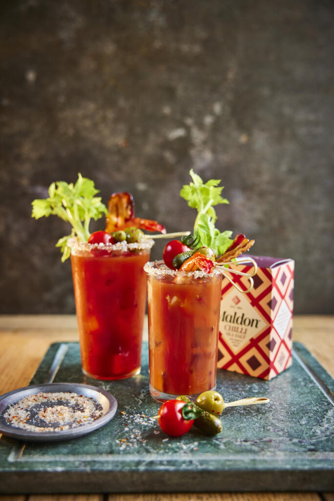 Loaded bloody Mary cocktail. Garnished include prawn tail, cherry tomato, stuffed olive, gherkin and a celery stick. Salt rim made from Maldon Chilli Sea Salt 100g pack.