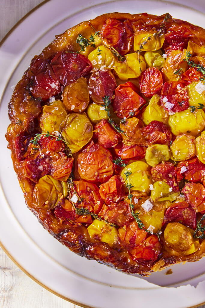 Cherry Tomato Tarte Tatin. A mixture of yellow, orange and red cherry tomatoes wrapped in pastry. Seasoned with Maldon Garlic Sea Salt flakes. On a white plate with a gold rim.