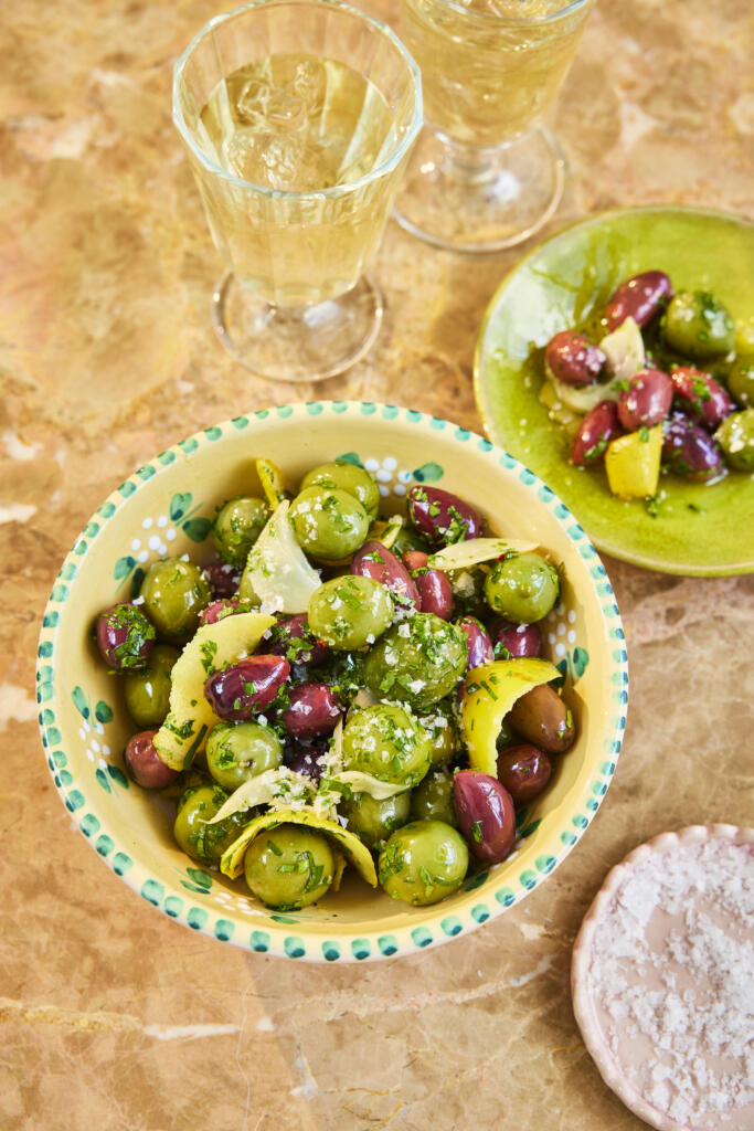 A bowl of homemade marinated olives with lemon peel and sea salt flakes.