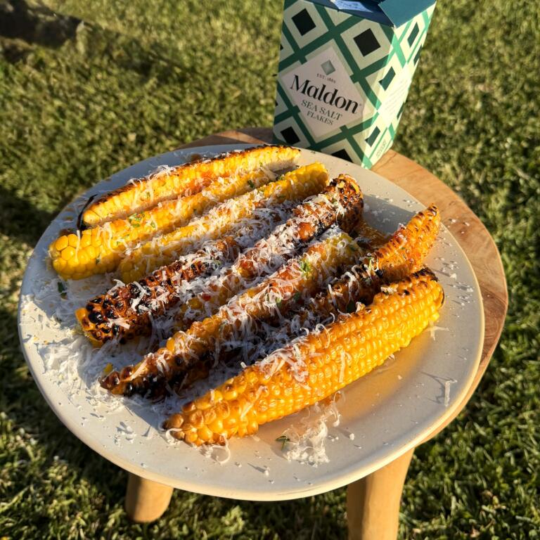 Fire-charred sweetcorn ribs topped with chilli lime butter, fresh coriander and grated Parmesan, served on a plate.